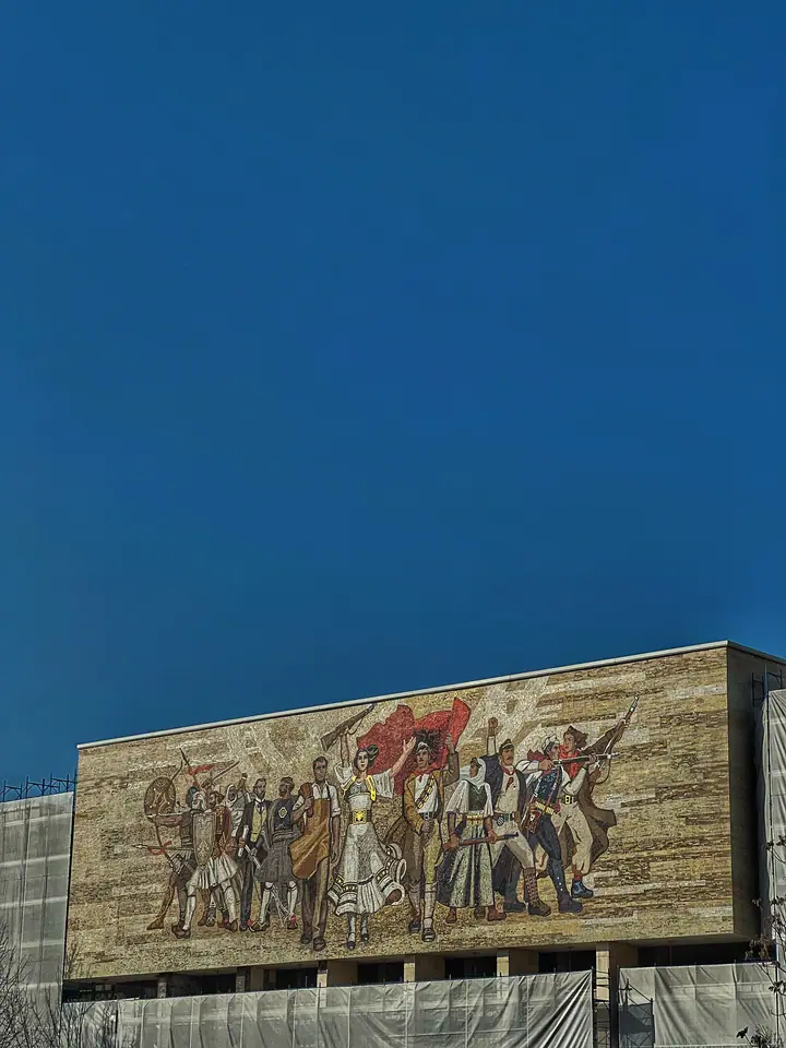 Tirana museum facade with socialist mural against a clear blue sky.
