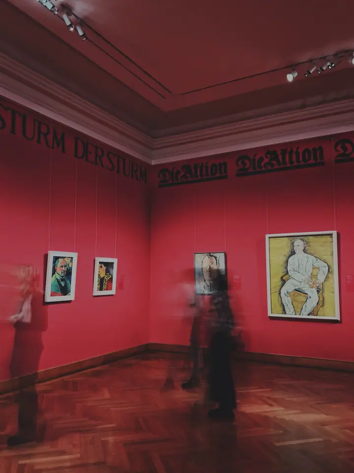 Blurred figures moving through a red Vienna museum room.